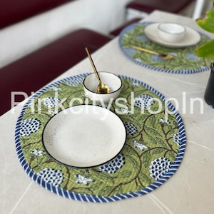 May include: A green and blue floral round placemat with a white plate and a small white bowl with a gold spoon on top.