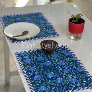 Può includere: Due tovagliette all'americana blu e bianche con un piatto bianco e una ciotola di legno su un tavolo bianco. Le tovagliette hanno un bordo a strisce blu e bianche.