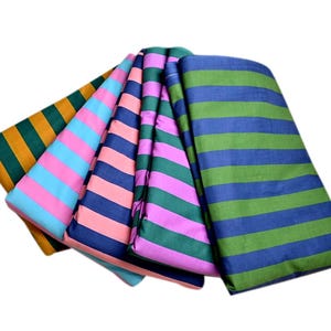 Puede incluir: Cinco muestras de tela a rayas en diferentes colores, incluyendo rosa, azul, verde y naranja. La tela está doblada y dispuesta en forma de abanico.