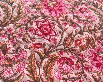 May include: Close-up of a quilted fabric with a floral pattern. The design features large, stylized red and pink flowers with green and yellow leaves on a light beige background. The quilting creates a diamond pattern.