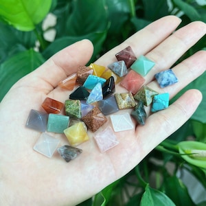 May include: A collection of small, colourful, pyramid-shaped crystals in various shades of red, green, blue, brown, white, and pink. The crystals are arranged on a hand, showcasing their unique shapes and textures.