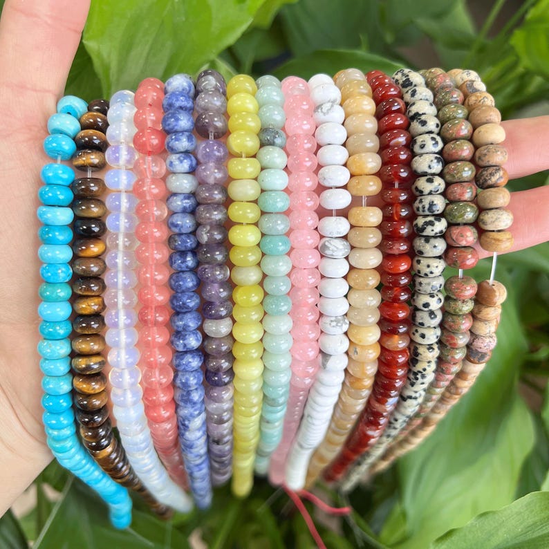 May include: A collection of 16 strands of gemstone beads in various colors, including turquoise, brown, pink, white, yellow, green, blue, and red. The beads are all round and have a smooth, polished finish.