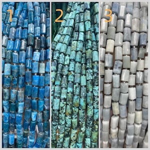 Puede incluir: Tres hilos de cuentas de piedras preciosas en tonos azul, turquesa y gris. Las cuentas son rectangulares con bordes redondeados y están ensartadas con espaciadores plateados. Las cuentas están dispuestas en filas verticales.