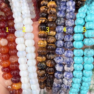 Op de afbeelding: Vijf strengen edelsteen kralen, elk met een andere kleur en patroon. De kralen zijn allemaal pompoenvormig. Van links naar rechts zijn de kleuren: rood, wit, bruin, blauw en turquoise.