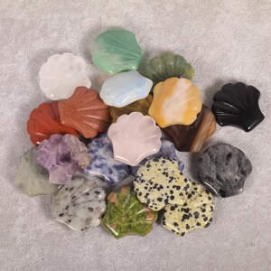 May include: A collection of gemstone seashell carvings in various colors. The carvings include white, green, red, pink, and black shells. The shells are made of different types of stones, including quartz, jade, and obsidian.