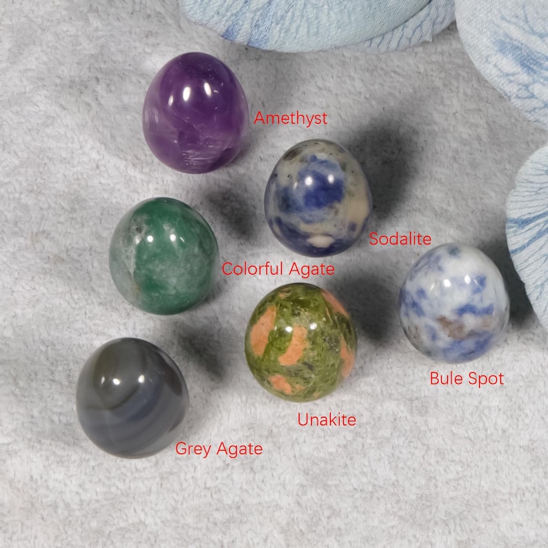 Puede incluir: Una colecci&oacute;n de esferas de piedras preciosas pulidas, incluyendo amatista, sodalita y unakita. Las esferas son de varios colores, como p&uacute;rpura, verde y gris. El texto indica el nombre de cada esfera.