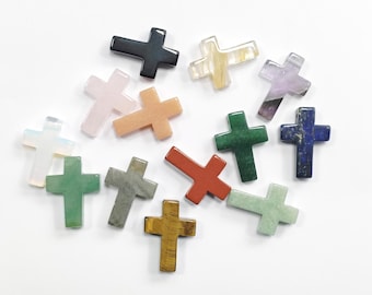 May include: A selection of gemstone crosses in diverse colours, such as green, red, blue, and pink. The crosses are crafted from various materials and have a polished finish. The crosses are arranged on a white surface.