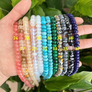 May include: A collection of 12 strands of beads, each with a different color and pattern. The beads are strung on a clear thread and are arranged in a row. The beads are numbered 26 through 37.