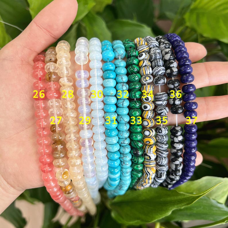 May include: A collection of 12 strands of beads, each with a different color and pattern. The beads are strung on a clear thread and are arranged in a row. The beads are numbered 26 through 37.