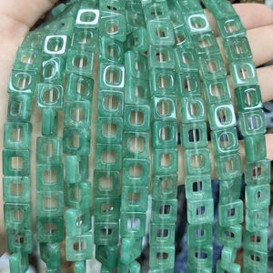 Puede incluir: Una hebra de cuentas de jade verde con forma cuadrada y un agujero en el centro de cada cuenta.