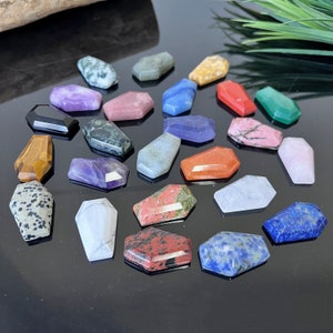 May include: A collection of 20 small, polished, gemstone coffin-shaped pendants in various colours, including red, blue, green, purple, black, white, and brown.