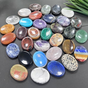 K&ouml;nnte beinhalten: Eine Sammlung von 25 glatten, polierten ovalen Steinen in verschiedenen Farben und Mustern. Die Steine bestehen aus verschiedenen Arten von Kristallen und Mineralien, darunter Amethyst, Rosenquarz, Tigerauge und Jaspis.