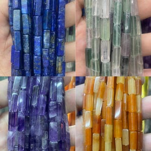 May include: A collection of four strands of rectangular beads in various colors including deep blue with gold flecks, translucent pale green, vibrant purple, and warm orange. Each strand features uniform, smooth, polished stone-like beads.