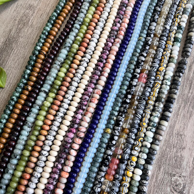 May include: A collection of 18 strands of colorful gemstone beads. The beads are round and have a variety of patterns and textures. The beads are arranged in a fan shape, with the strands overlapping each other.