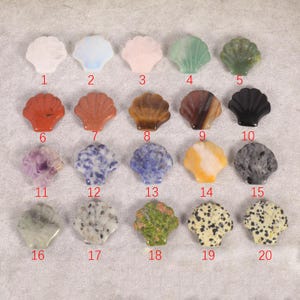 May include: A collection of twenty seashell-shaped gemstones in various colors and patterns. The gemstones include white, blue, pink, green, red, brown, black, purple, and speckled designs. Each stone is numbered from 1 to 20.