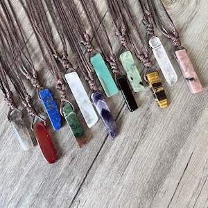Könnte beinhalten: Eine Sammlung von 14 verschiedenen farbigen Edelstein-Anhängern an braunen Lederbändern. Die Edelsteine umfassen Amethyst, grüner Aventurin, klarer Quarz, roter Jaspis, Lapislazuli, Tigerauge und Rosenquarz.