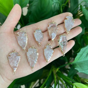 May include: Ten gold-plated arrowhead shaped pendants with clear quartz crystals. The pendants are approximately 5 cm long and have two jump rings for attaching to jewellery.