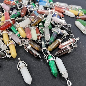 May include: A collection of colorful crystal point pendants with silver metal caps and loops. The pendants are made of various types of gemstones, including amethyst, rose quartz, tiger's eye, and green aventurine.