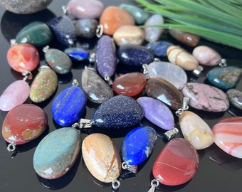 May include: Assortment of colorful gemstone pendants, each with a silver bail. The stones are in various shapes and sizes, including teardrop, oval, and round. The colors include red, blue, green, purple, brown, and white.