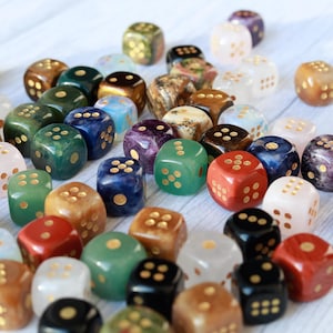 May include: A collection of colorful dice in various colors, including green, red, blue, and white. Each die has gold-colored dots. The dice are made of different materials, creating a variety of textures and patterns.