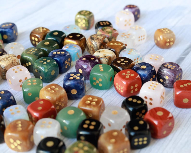 May include: A collection of colorful dice in various colors, including green, red, blue, and white. Each die has gold-colored dots. The dice are made of different materials, creating a variety of textures and patterns.