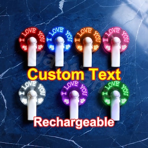 May include: A collection of rechargeable LED fans in various colors, each displaying the text "I LOVE YOU" in a circular pattern. The image also includes the words "Custom Text" and "Rechargeable".