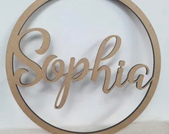 May include: A wooden circle with the name "Sophia" written in a cursive font. The name is cut out of the wood and is attached to the circle.