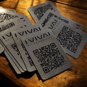 Könnte beinhalten: Ein Stapel silberner Metall-Visitenkarten mit einem schwarz-weißen QR-Code und dem Text "I VIVAI AL PARRUCCHIANO" auf jeder Karte.