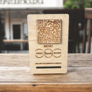 Può includere: Un cartello in legno con un codice QR, le parole "MENU" e "Timothy", e il testo "Coffee" e "Kitchen" in cerchi. Il cartello dice anche "10% di sconto per gli ospiti di Romello".