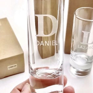 Può includere: Due bicchieri da shot in vetro trasparente con una lettera bianca e un nome incisi sul davanti. Il bicchiere a sinistra ha la lettera "D" e il nome "DANIEL" incisi. Il bicchiere a destra ha la lettera "L" e il nome "LAZAR" incisi.