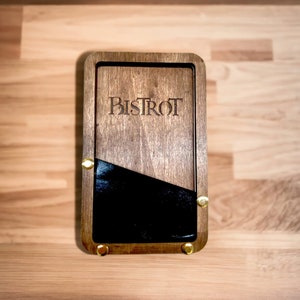 Può includere: Una scatola di legno con interno nero e dettagli in ottone. La scatola è incisa con la parola "Bistrot".