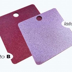 Può includere: Due pezzi quadrati di carta testurizzata con un foro al centro. La carta a sinistra è di colore bordeaux scuro ed è etichettata "lato B". La carta a destra è di colore lavanda chiaro ed è etichettata "lato A".