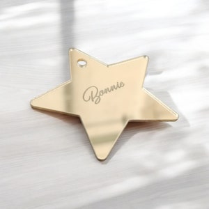 May include: A gold-colored star-shaped tag with a small hole at the top. The name "Bonnie" is elegantly engraved on the surface. The tag is likely made of metal and has a reflective finish.