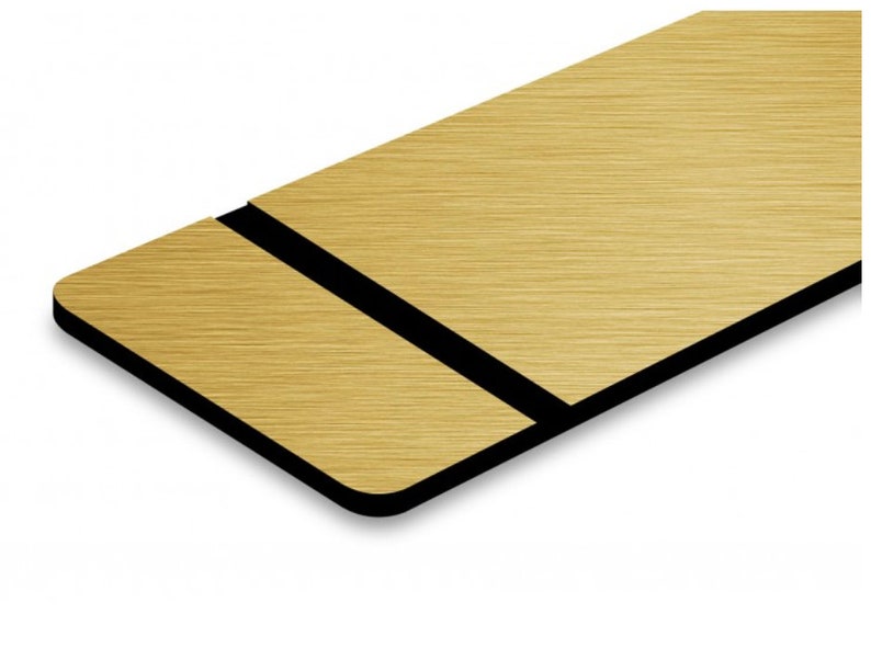 May include: A gold brushed metal sign with a black border. The sign is rectangular and has a brushed metal finish.