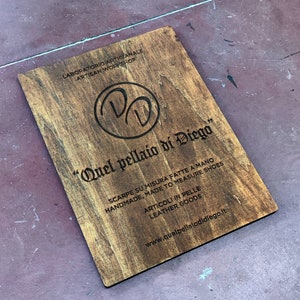 Könnte beinhalten: Ein Schild aus Holz mit dem Text "Quel pellaio di Diego" in einer dekorativen Schriftart. Das Schild enthält auch den Text "Laboratorio Artigianale Artisan Workshop", "Scarpe su misura fatte a mano Handmade, Made to Measure Shoes", "Articoli in pelle Leather Goods" und "www.quelpellaiodidiego.it".