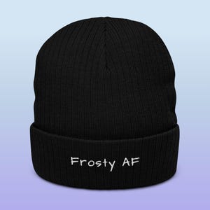 Może przedstawiać: Czarna wełniana czapka z białym haftem "Frosty AF" na mankiecie.