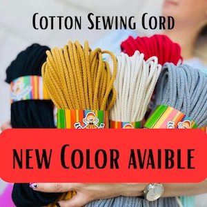 Peut inclure: Plusieurs bobines de cordon de couture en coton de couleurs variées, dont noir, jaune moutarde, crème, rouge et gris. Le texte "Cotton Sewing Cord" est en haut et "NEW COLOR AVAIBLE" sur une bannière rouge. Chaque bobine est emballée avec une étiquette colorée.