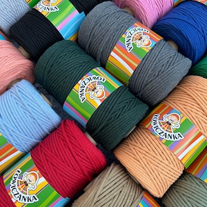 Könnte beinhalten: Eine Sammlung farbenfroher Makramee-Kordelspulen in verschiedenen Farbtönen, darunter Rosa, Blau, Grün und Rot. Jede Spule ist mit einem Etikett mit einer Cartoonfigur und dem Markennamen versehen. Die Kordeln sind eng gewickelt, was auf ein hochwertiges Bastelmaterial hindeutet.