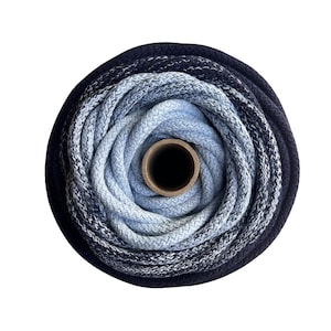 May include: A spool of braided cord featuring a colour gradient that transitions from a dark navy blue on the outer edge to a light sky blue in the centre. The cord is wound tightly around a central cardboard tube, creating a circular pattern.
