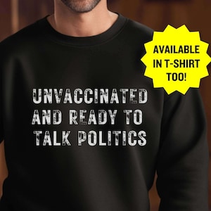 May include: Black sweatshirt with white text that reads "Unvaccinated and Ready to Talk Politics". The text is distressed and has a vintage look. A yellow starburst sticker is in the top right corner that reads "Available in T-shirt Too!"