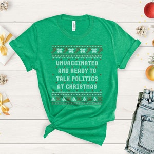 以下が含まれることがあります： クリスマスセーターのデザインが施された緑色のTシャツで、「ワクチン未接種でクリスマスに政治について話す準備ができています」と書かれています。
