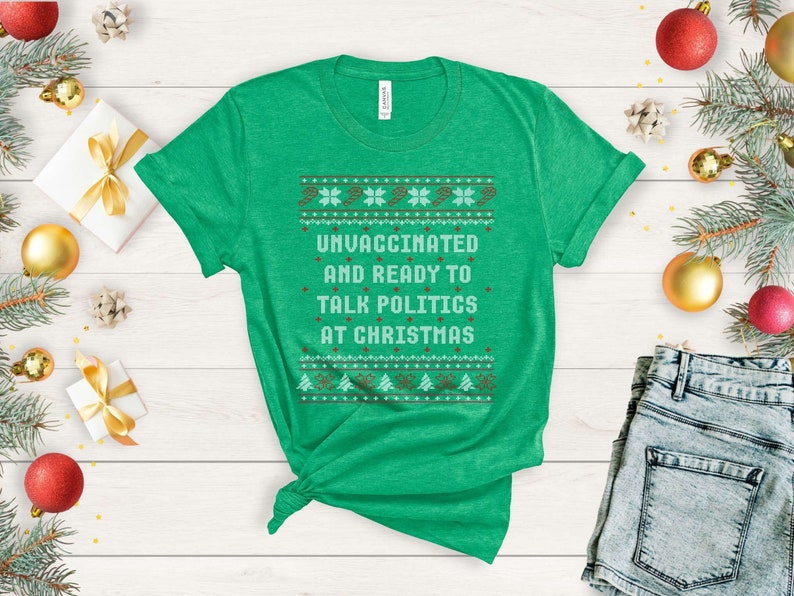以下が含まれることがあります： クリスマスセーターのデザインが施された緑色のTシャツで、「ワクチン未接種でクリスマスに政治について話す準備ができています」と書かれています。