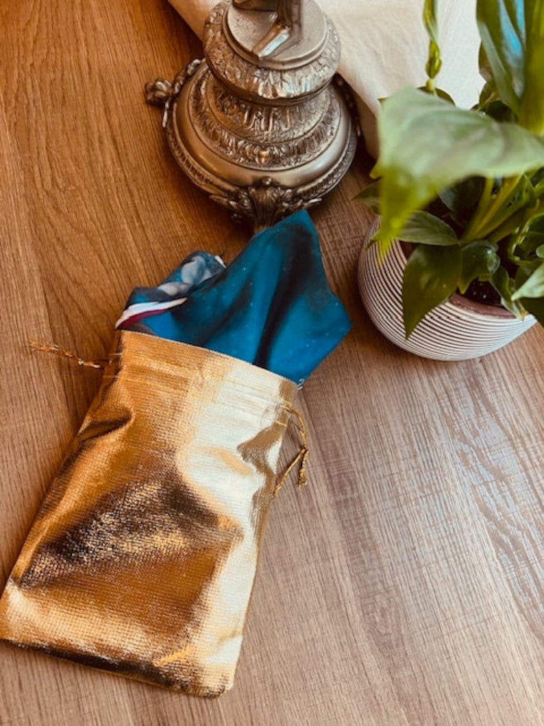 May include: A gold drawstring bag with a teal blue and white patterned fabric inside. The bag is sitting on a wooden surface.