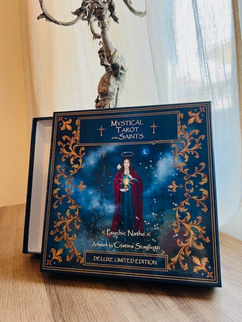 May include: A blue box with gold accents and the text "Mystical Tarot of the Saints" and "Psychic Nathe" with artwork by "Cristina Staglioti" and "Deluxe Limited Edition".