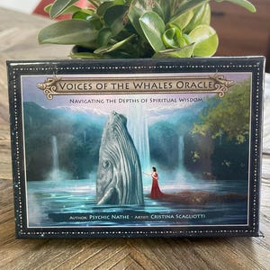 Puede incluir: Una baraja de oráculo en caja titulada "VOICES OF THE WHALES ORACLE" con el subtítulo "NAVIGATING THE DEPTHS OF SPIRITUAL WISDOM". La obra de arte representa una ballena en el agua con una cascada y una persona con un vestido rojo. Autor: Psychic Nathe, Artista: Cristina Scagliotti.