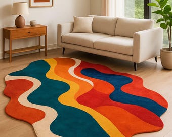 May include: A colorful, abstract area rug with a unique, organic shape. The rug features flowing bands of red, orange, yellow, teal, blue, and cream. The rug is placed on a hardwood floor in a living room setting.