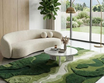 May include: A modern living room featuring a cream-colored curved sofa with two round pillows, a marble-topped coffee table, and a green rug with a landscape design. A gold arched floor lamp and large windows offer a view of the outdoors.
