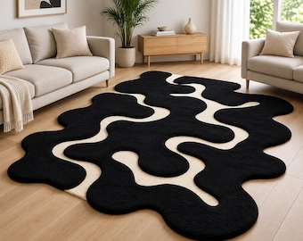Puede incluir: Una alfombra grande con una forma orgánica irregular y audaz con un diseño de alto contraste. La alfombra consta de secciones negras gruesas y afelpadas que se entrelazan con una base de color crema suave, creando un patrón fluido y abstracto.