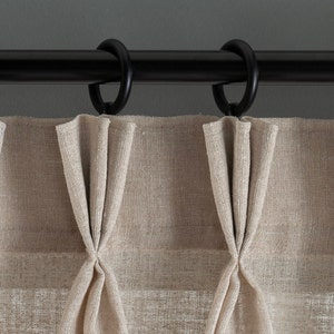 May include: Beige curtains with pleats hanging from a black curtain rod with rings.