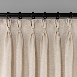 Pode incluir: Cortinas bege com um padrão sutil de espinha de peixe, penduradas em uma haste de cortina preta com argolas prateadas.